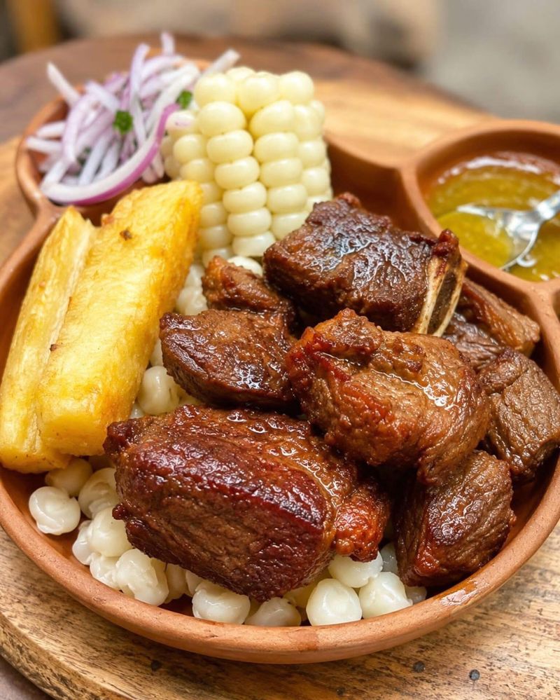 Crispy pork with choclo corn, mote, fried yuca and salsa criolla in a clay dish