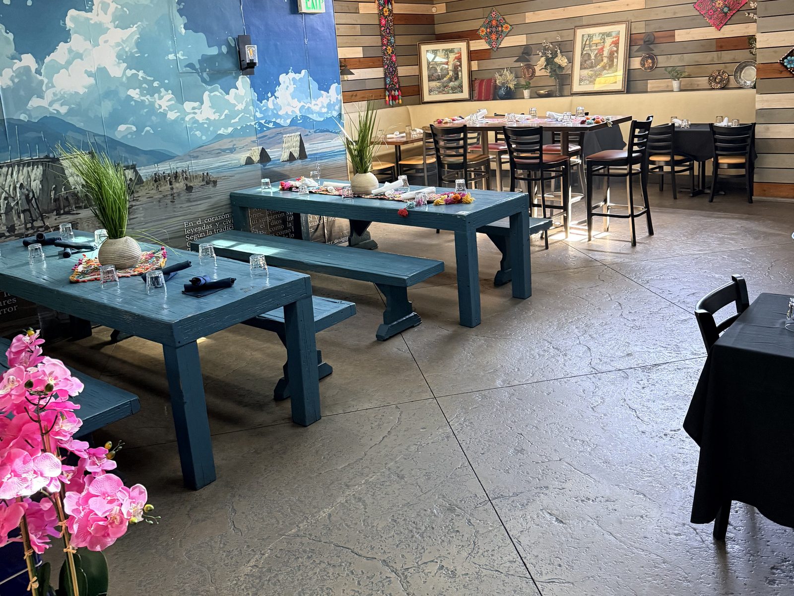 Coya's dining room with blue wood tables, black tablecloths and a sky mural